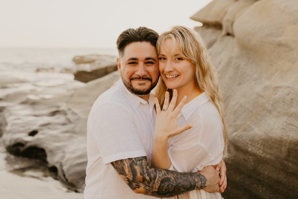 Couple holding each other while showing off an engagement ring.