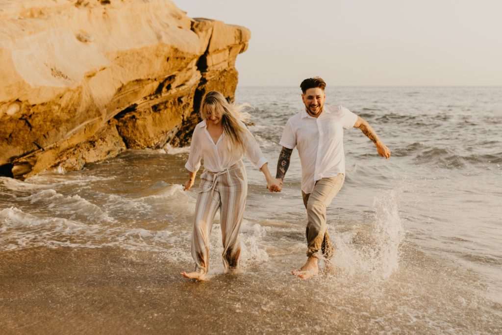 Newly engaged couple running along the shore at Ocean Beach in San Diego.