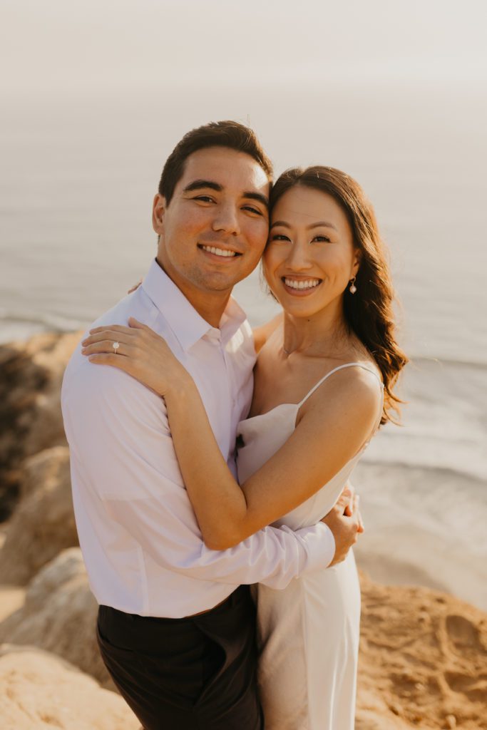 Engaged Asian couple smiling at the camera in Torrey Pines