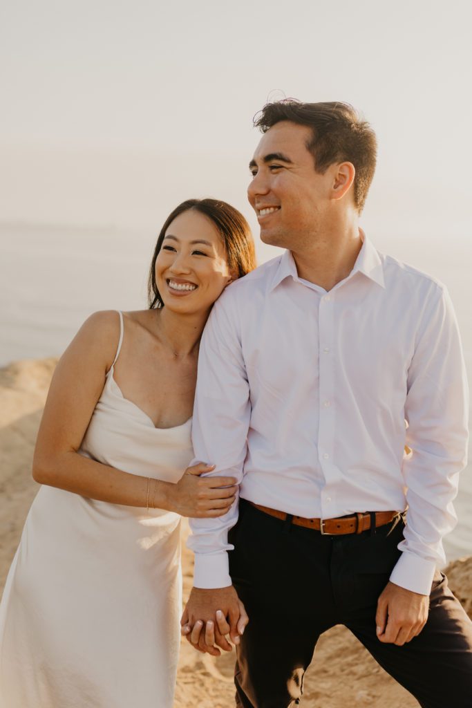 Engaged Asian couple smiling in the distance in Torrey Pines