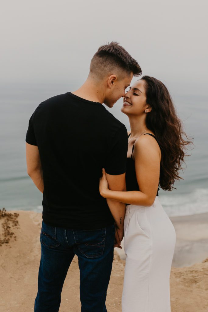Couple leaning in for a kiss at Torrey Pines Gliderport overlooking the water.