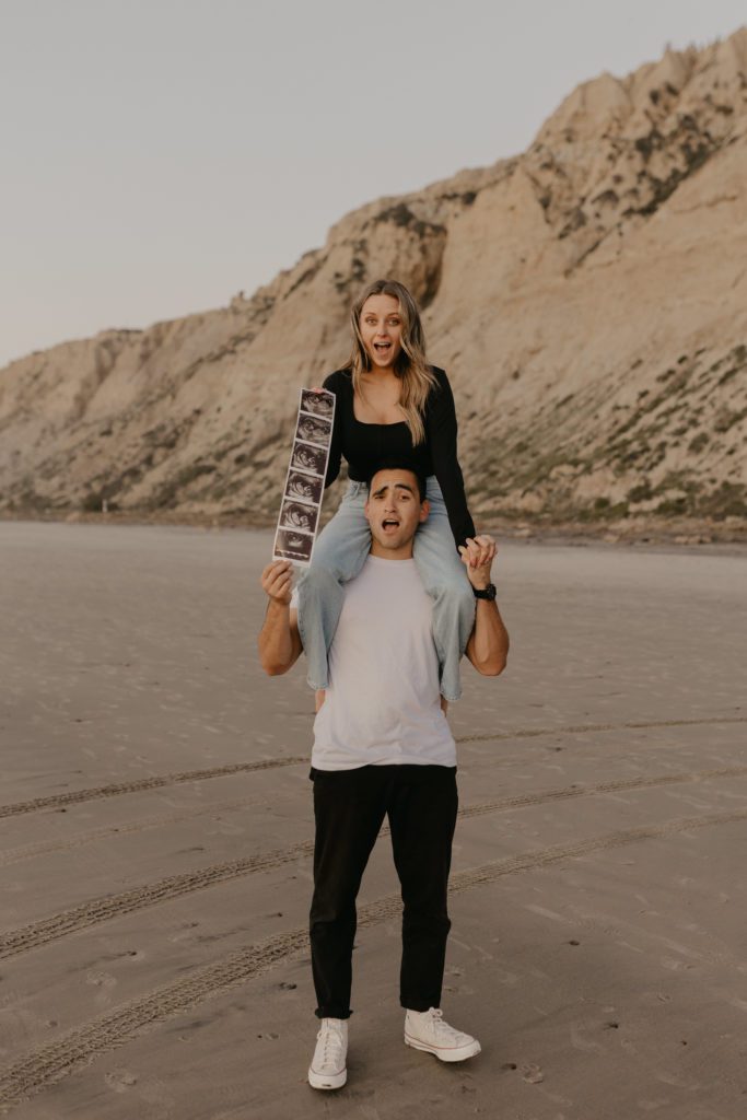 Couple making surprised faces while holding up a pregnancy ultrasound.