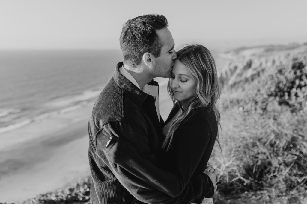 black and white photo of a man kissing woman on the forehead while hugging