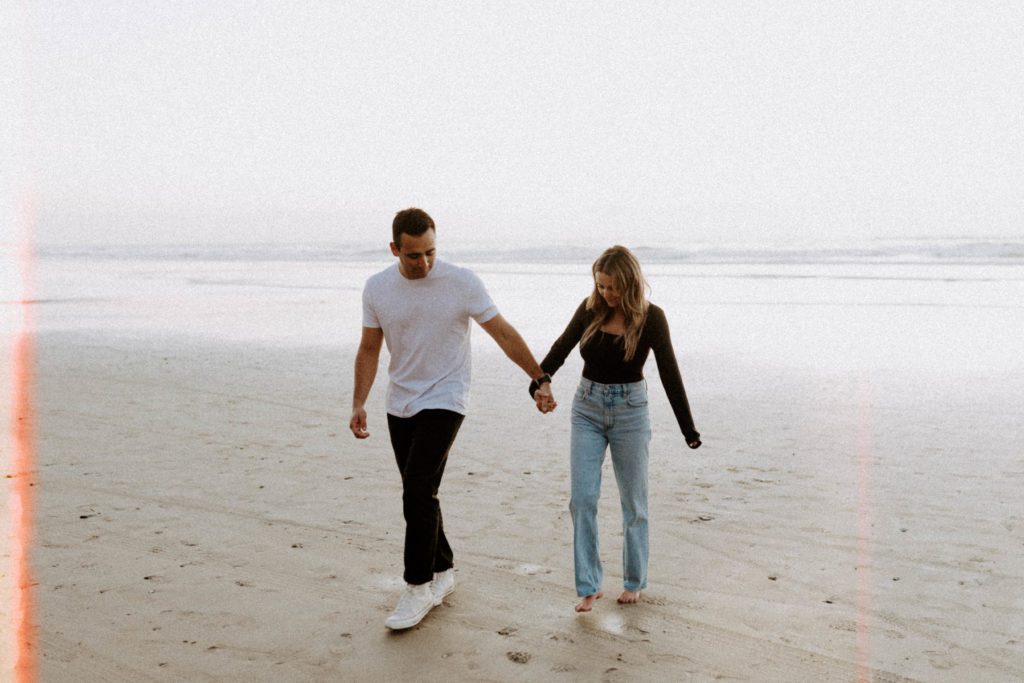 Couple walking along the beach during a pregnancy announcement photoshoot.